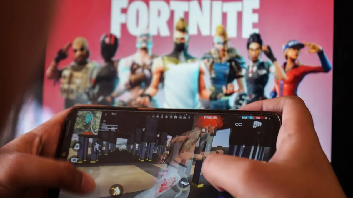 Ein Kind spielt ein Spiel auf einem Mobiltelefon mit einem Bild des Fortnite–Spiels auf dem Computerbildschirm im Hintergrund. (zu dpa: „Apple wirft Account von „Fortnite“-Firma Epic aus dem App Store»)
