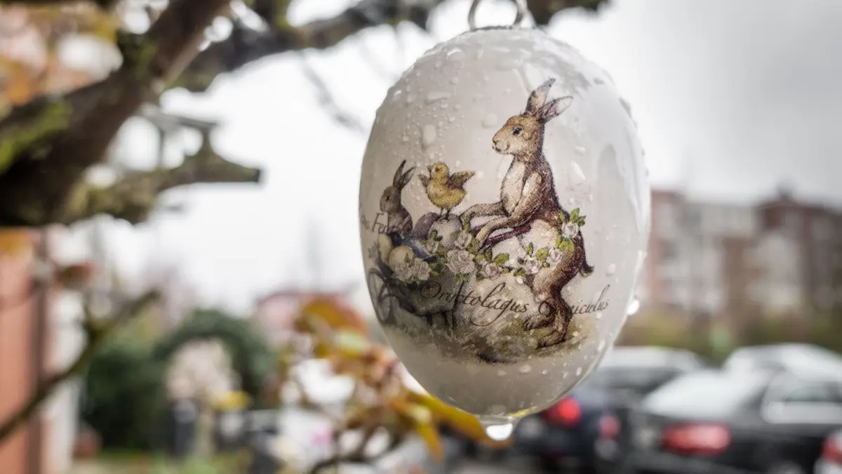 Die Eiersuche fällt am Ostermontag wohl ins Wasser.: ARCHIV - 07.04.2023, Hessen, Frankfurt/Main: Ein mit einem Hasenmotiv bedrucktes Porzellan-Osterei hängt im Regen vor einem Hauseingang. (zu dpa: «Regen am Ostermontag») Foto: Frank Rumpenhorst/dpa +++ dpa-Bildfunk +++