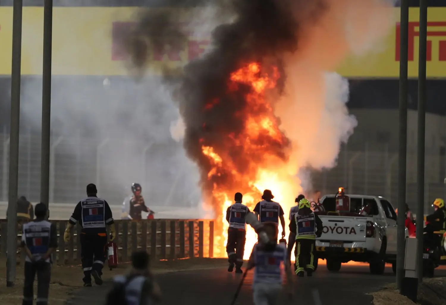 Marshalls laufen zur Unfallstelle und löschen das Auto von Romain Grosjean aus Frankreich vom Team Haas. Romain Grosjean war kurz nach dem Start mit seinem Auto in die Leitplanken gekracht.