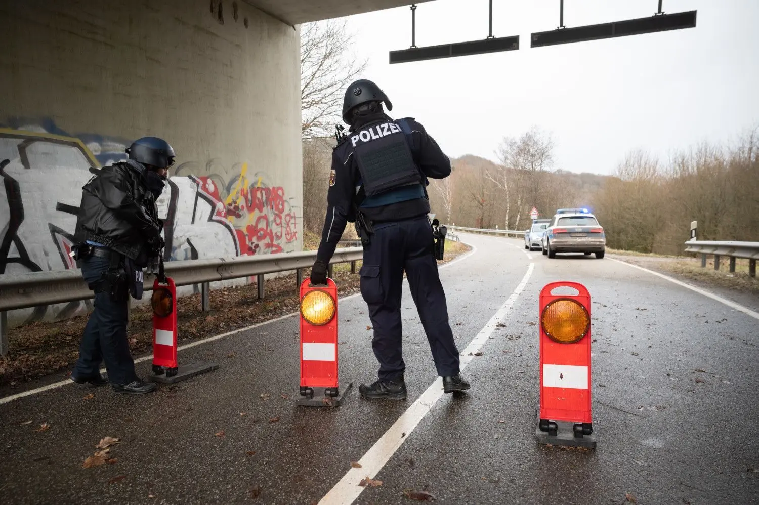 Polizeibeamte stehen an einer Absperrung an der Kreisstraße 22 rund einen Kilometer von dem Tatort, an dem zwei Polizeibeamte durch Schüsse getötet wurden.