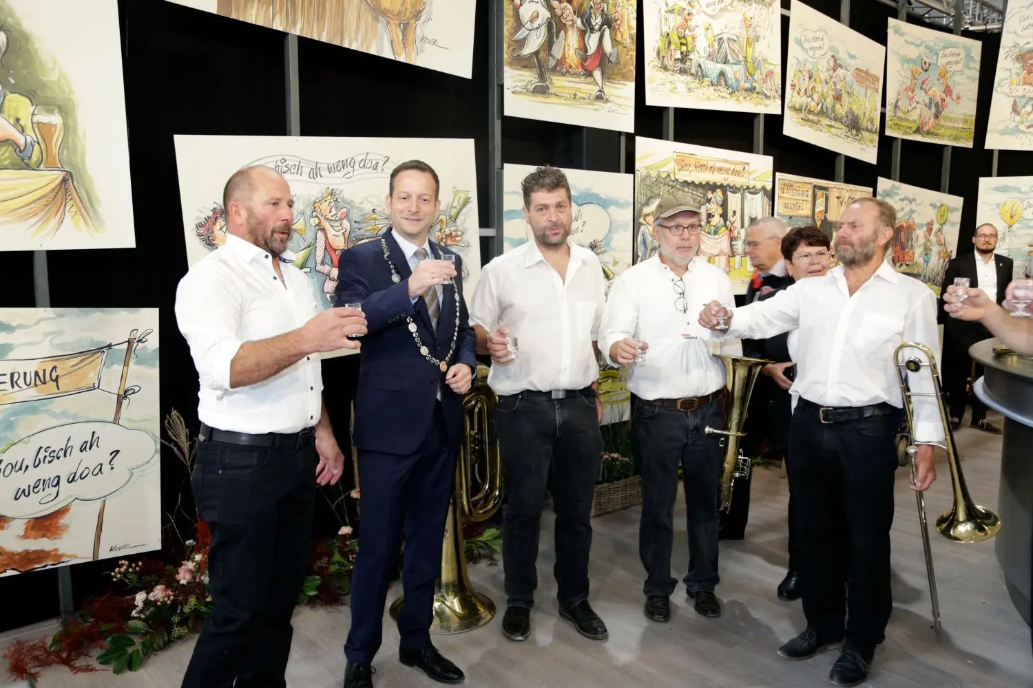 Nach dem offiziellen Teil gibt’s für Bürgermeister Dr. Sebastian Kampe (mit Amtskette) ein Schnäpsle mit den „Roader Schnäpsle“ vor der Kulisse der Muswiesen-Szenen von Darius Kovalik.