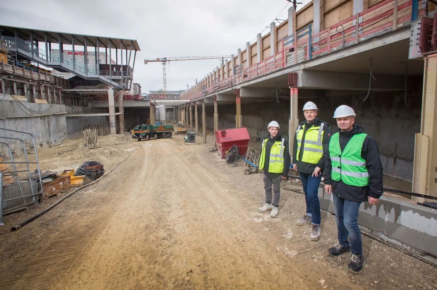 Koordinator Harald Walter (von rechts) und die Bauleiter Frank Bunz und Jan Heintz in der Baugrube der Tiefgarage am Bahnhof (links der Steg). Auf dem Deckel (rechts) fahren Straßenbahn und Busse.