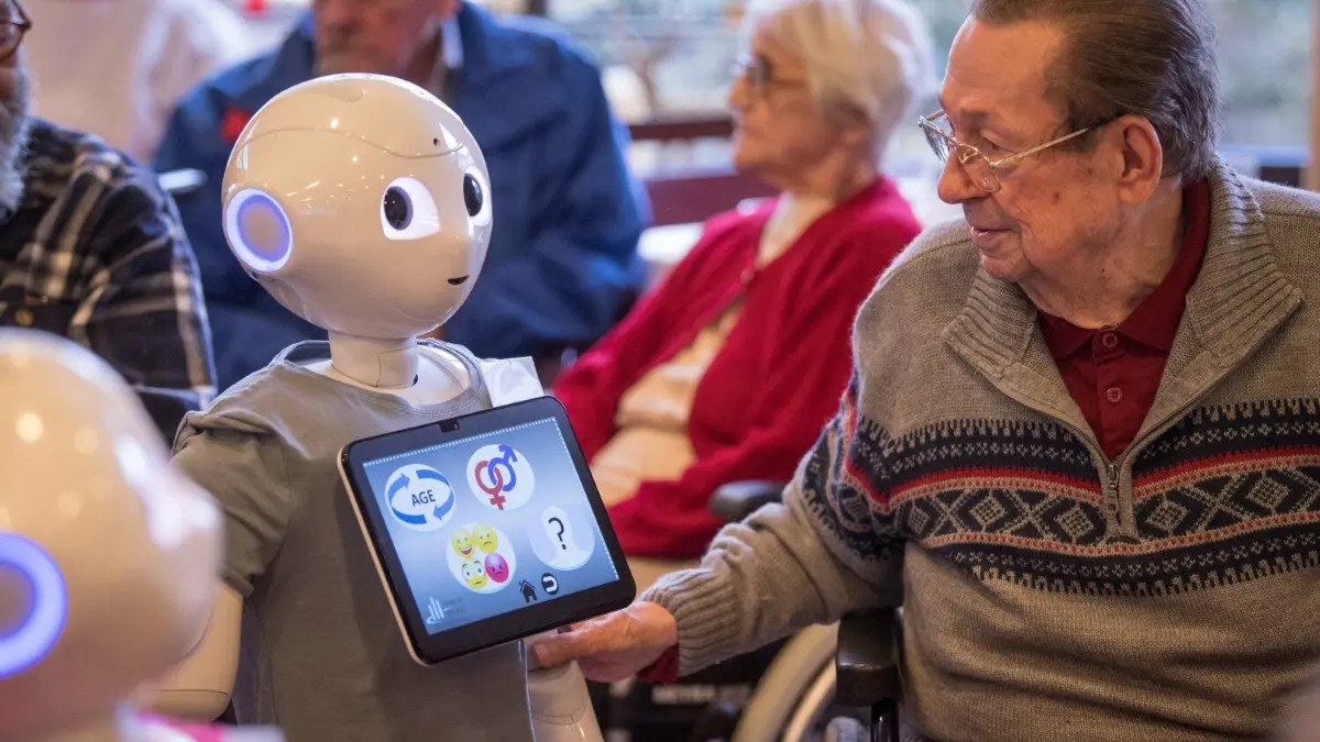 Der Roboter "Pepper" wird unter anderem in Alten- und Pflegeheimen als Quizmaster und Entertainer eingesetzt.
28.11.2018, Hessen, Frankfurt/Main: Auf Tuchfühlung mit dem humanoiden Roboter "Pepper" geht der 81-jährige Helmut Brieger, Bewohner eines Alten- und Pflegeheims, während einer Informationsveranstaltung. Im Rahmen eines Projektes der University of Applied Sciences Frankfurt wollen die Studenten herausfinden, welche Wünsche Senioren an die Roboter haben, damit diese vielleicht eines Tages in Altersheimen eingesetzt werden können. Foto: Boris Roessler/dpa +++ dpa-Bildfunk +++