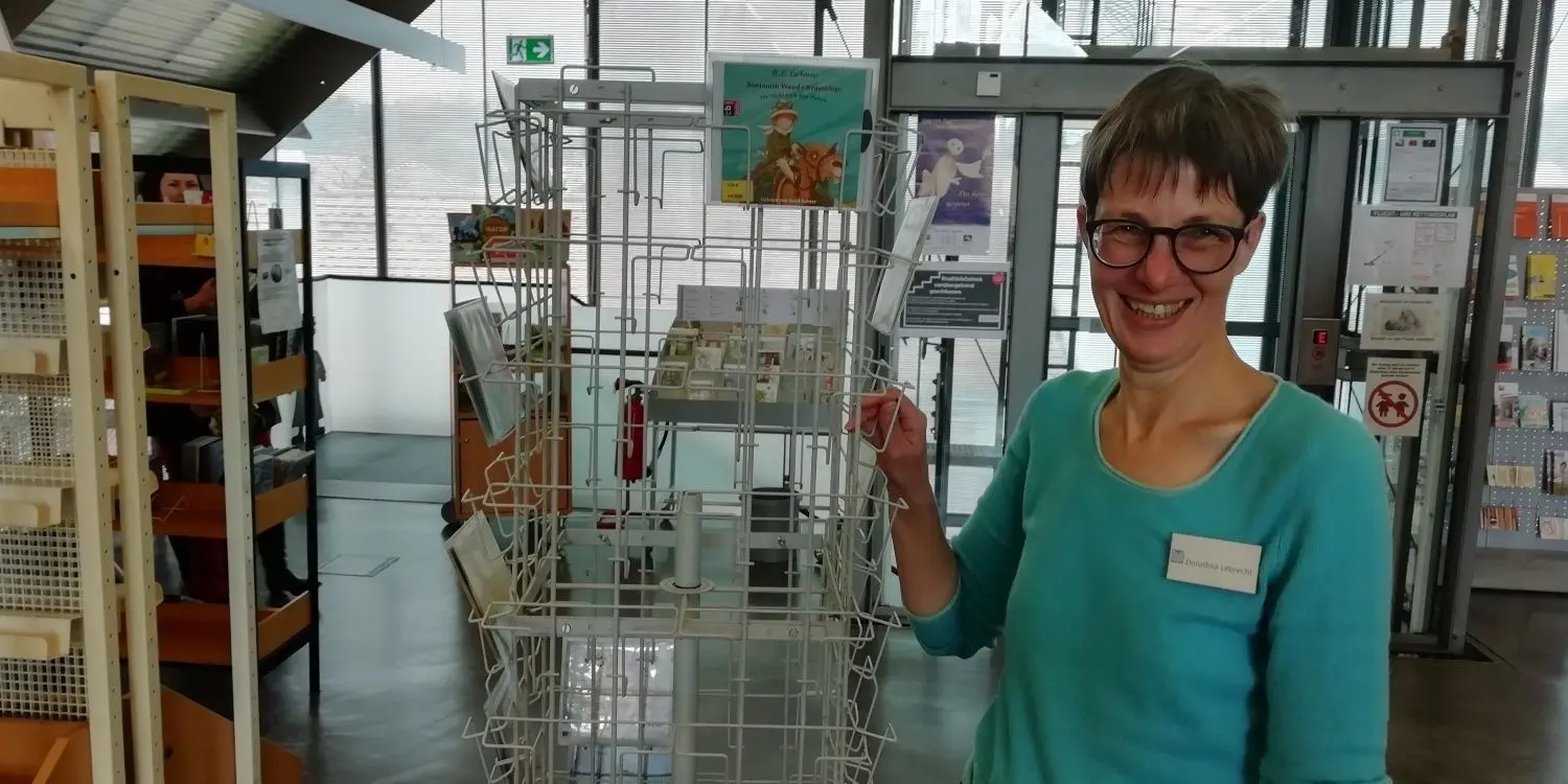 Ausgeliehen: Dorothea Lebrecht von der Stadtbibliothek zeigt einen leeren Schauständer. In Regalen stehen aber noch Bücher.