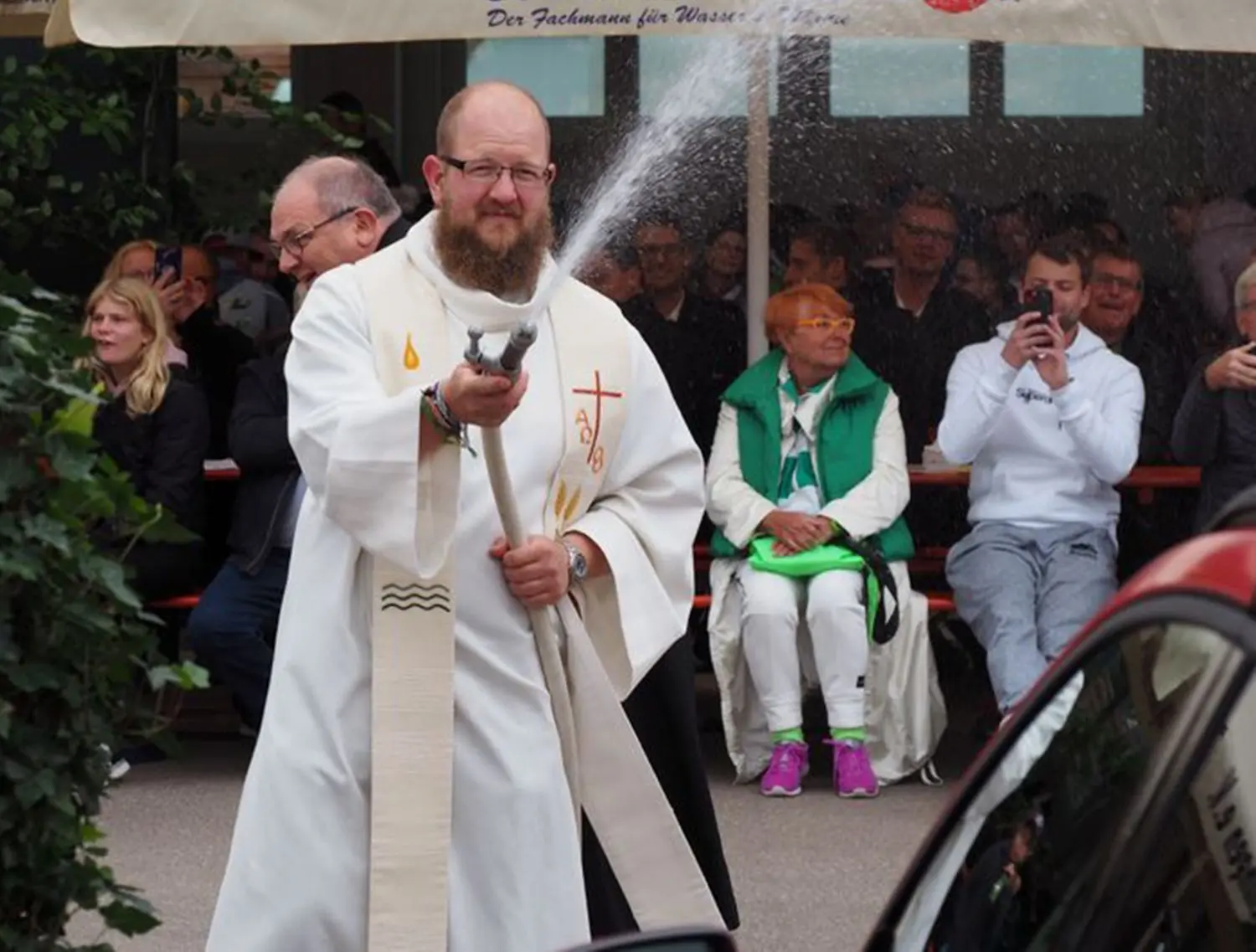 Kooperator Klaus Käfer durfte die Weihe der neuen Fahrzeuge der Hechinger Feuerwehr mit der Kübelspritze vornehmen. Er und Pfarrer Frank Steiner (im Hintergrund) hatten am Sonntag sichtlich Spaß an ihrer Aufgabe.