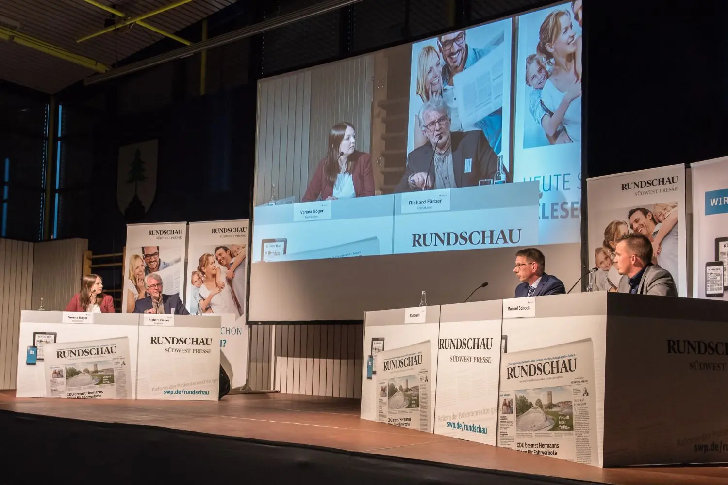Die beiden Moderatoren Verena Köger und Richard Färber (links) löchern die Kandidaten Ralf Glenk und Manuel Schock (rechts außen im Bild) mit Fragen. Wer gerade spricht, wird auf dem großen Bildschirm angezeigt.⇥