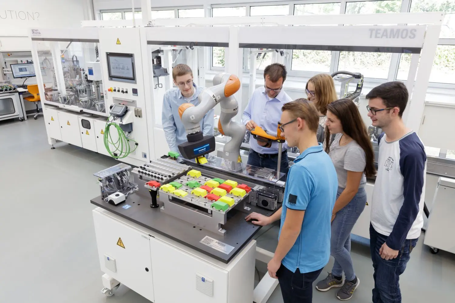 Oberstudienrat Mario Keppler, Ingenieur für Mechatronik, (Mitte) und Schüler des Technischen Gymnasiums in der Lernfabrik 4.0. Sie lernen die Funktionsweise eines  Roboters kennen, der in unmittelbarer Nähe zum Menschen und mit ihnen arbeiten kann.⇥