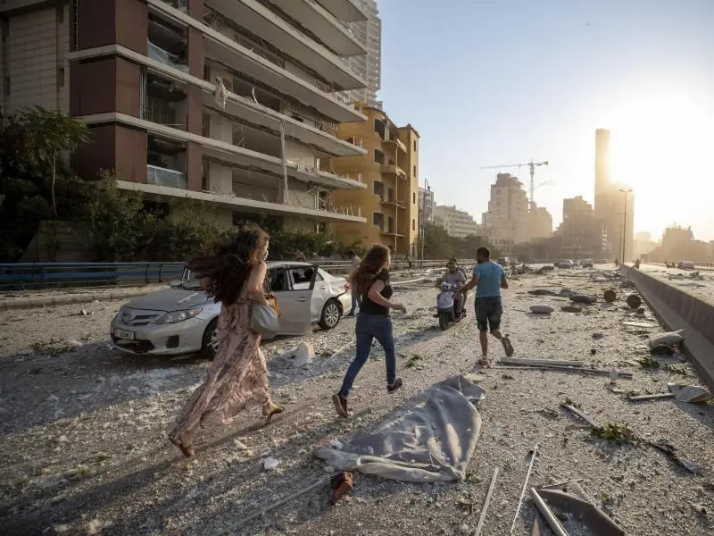 Menschen laufen nach der Explosion über eine von Trümmern übersäte Straße.