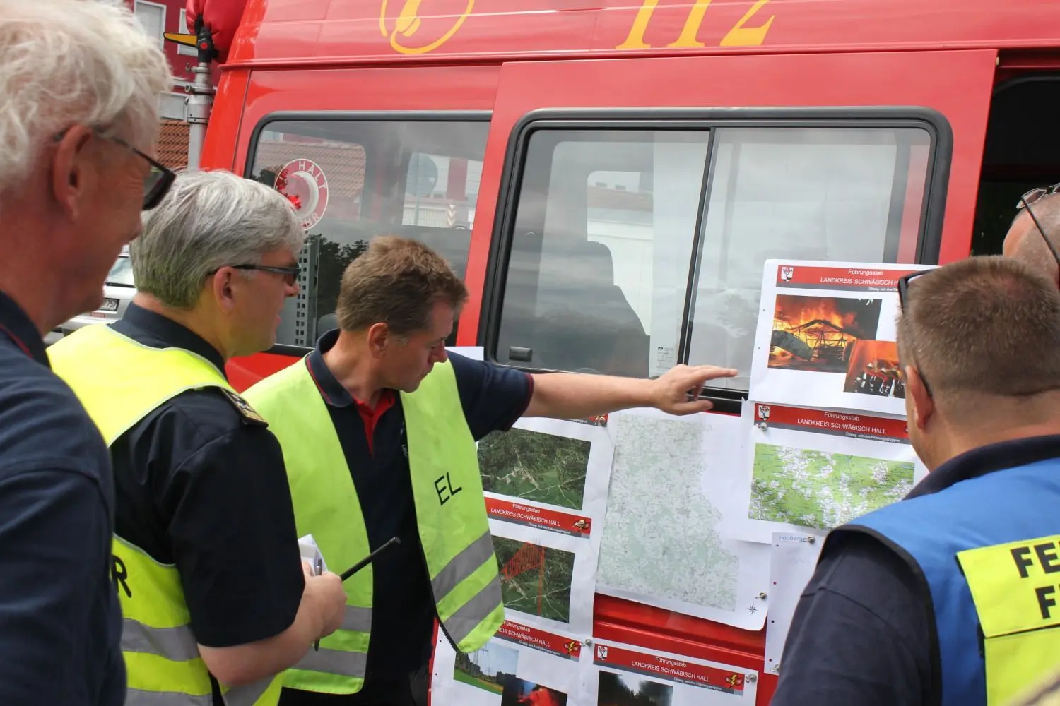 Der örtliche Einsatzleiter Dieter Butz (Dritter von links) erläutert dem Technischen Einsatzleiter Armin Klingenbeck die Lage in Gaildorf, wo ein Trafobrand bekämpft wird und bei Bühlerzell eine Schreinerei in Brand geraten ist. Übungs-Organisator Joachim Hägele (links) beobachtet das Geschehen.⇥