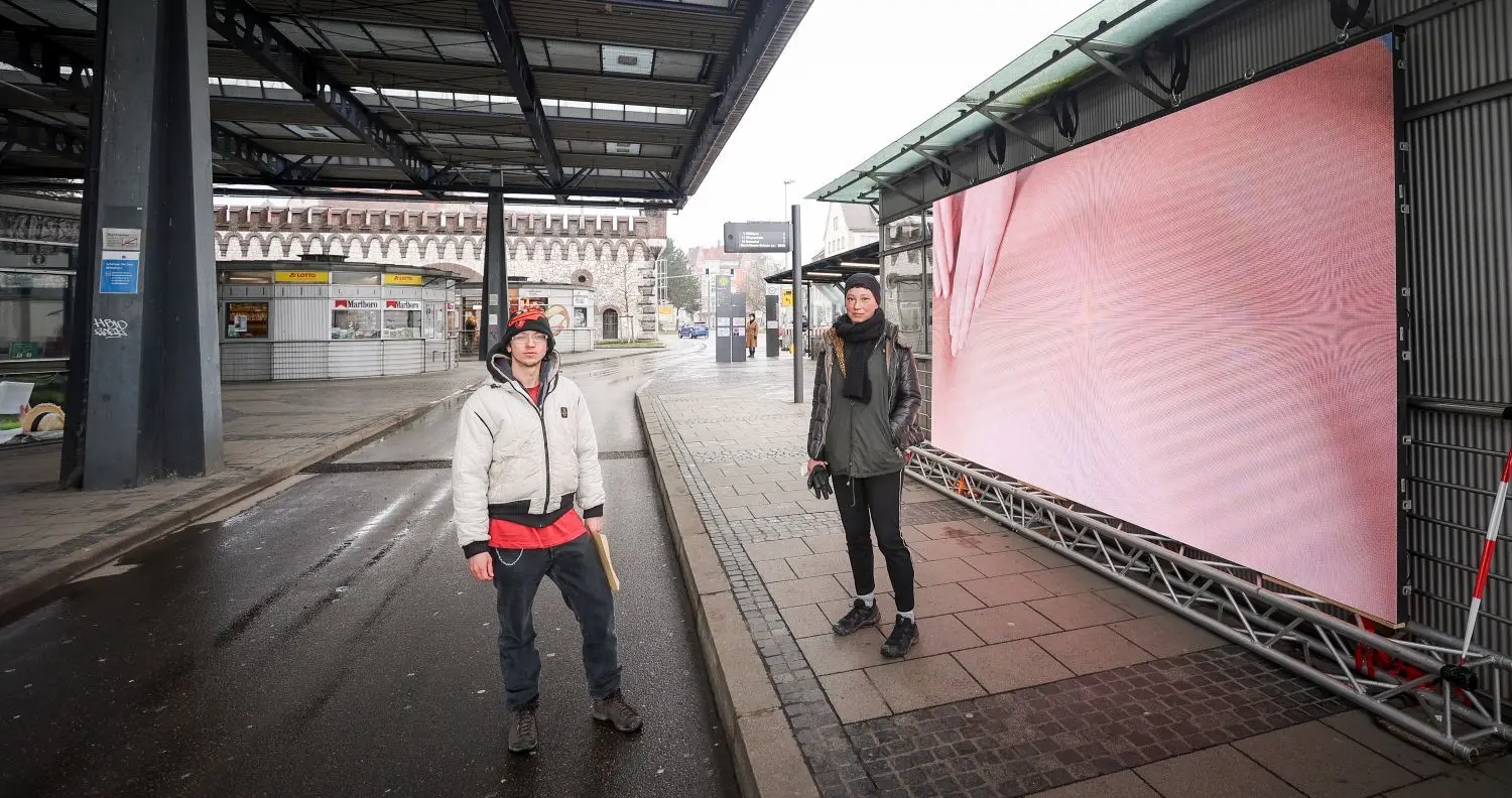 Die beiden Künstler Susanne Hopmann und Lukas Pfalzer stehen vor ihre Video-Installation an der Haltestelle Ehinger Tor.