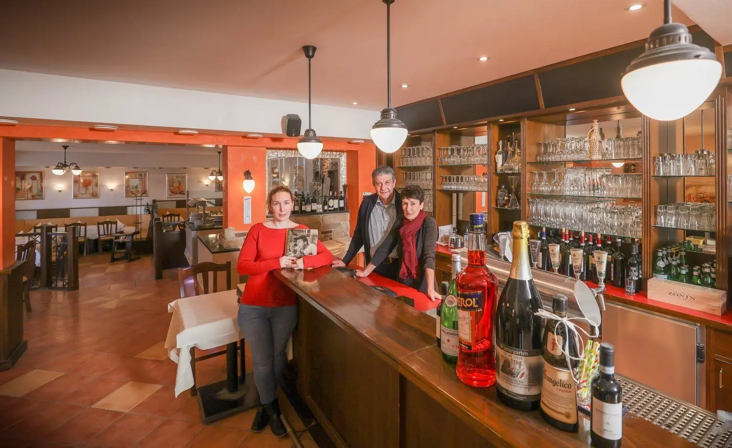 Noch stehen sie hinter der Theke: Angelo und Claudia Sarao mit ihrer ältesten Tochter Sarah. Zwischen diesen Wänden haben sie viel erlebt. Sie alle sind dankbar für die schönen Jahre und Erinnerungen in ihrem Restaurant.   ⇥