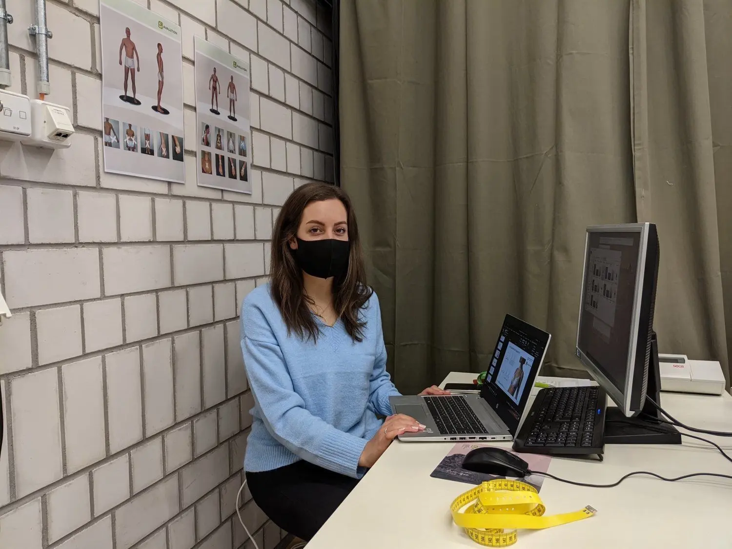 Elena Brake vom Forschungsprojekt „Your Bra“ der Fakultät Textil & Design. Hinter dem grünen Vorhang versteckt sich die 3D-Scan-Kabine. Ganz ohne Maßband geht es aber auch nicht. ⇥