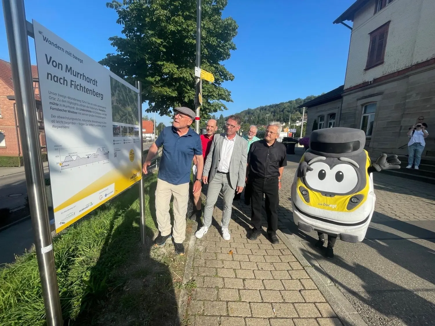 Winfried Hermann studiert die Hinweistafel am Murrhardter Bahnhof. Daneben: Gernot Gruber, Ralf Glenk, Werner Diederich, Walter Hieber und Maskottchen Bine. ⇥