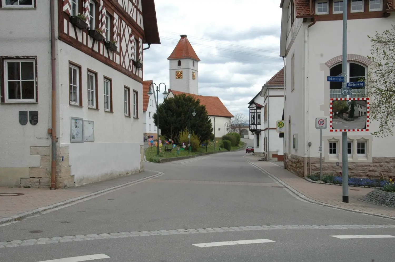 Die Weilheimer Ortsmitte derzeit: links vorne das Rathaus, hinten die Kirche, auf der rechten Seite die Alte Schule, die ehemalige Lehrerwohnung (jetzt Jugendraum), anschließend (Haus mit Erker) der „Adler“. Das Pfarrhaus, Sitz der Ortschaftsverwaltung, ist auf dem Foto verdeckt.⇥