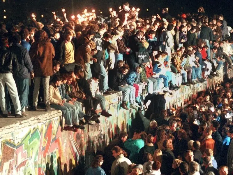 Jubelnde Menschen sitzen mit Wunderkerzen auf der Berliner Mauer.