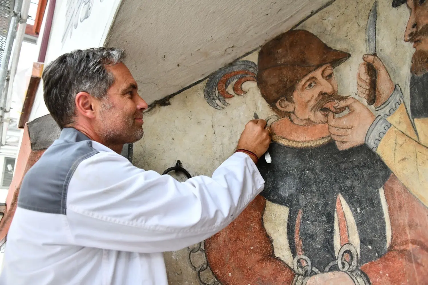 Kirchenmalermeister Meinrad Kopp bei der Arbeit an der Fassade des historischen Rathauses. Zunächst wird der Schmutz entfernt, dann Schäden ausgebessert – zum Schluss erhalten die Farben, hier im Pranger, eine Auffrischung. ⇥