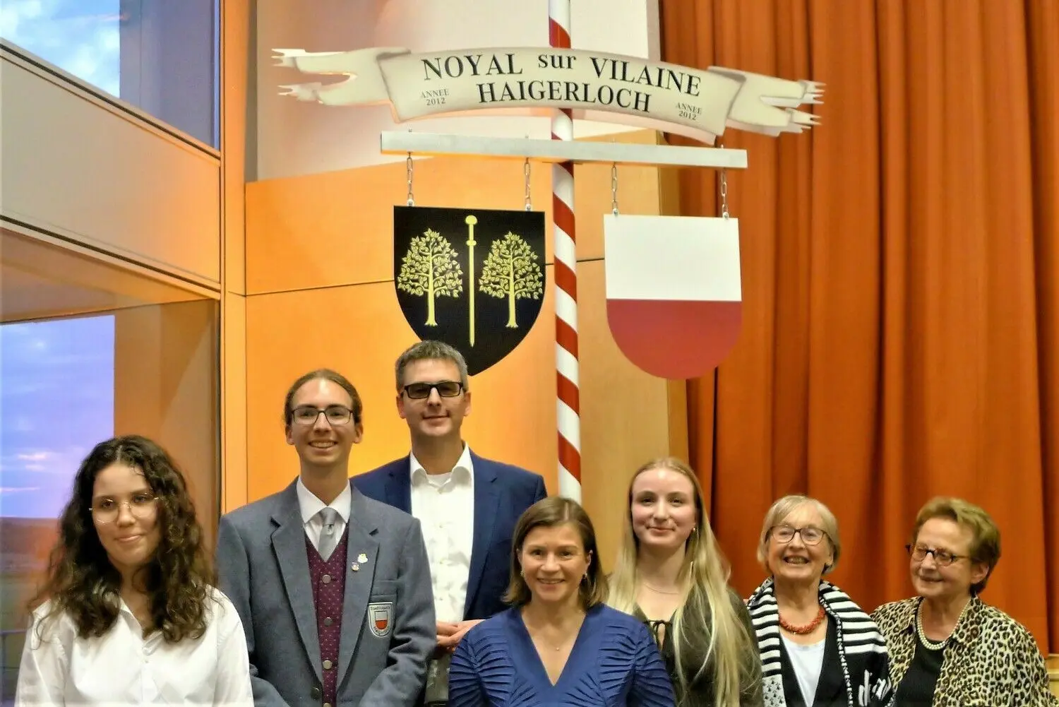 Geschenk an Noyal: ein Freundschaftspfahl mit den beiden Stadtwappen. Auf dem Foto (v. l.) die Moderatoren Élise Le Meur und Jannis Pfeffer, Bürgermeister Heiko Lebherz, Bürgermeisterin Marielle Muret-Baudoin, Moderatorin Sinah Sprissler sowie Angelika Pieper und Francoise Clanchin von den Partnerschaftsvereinen.