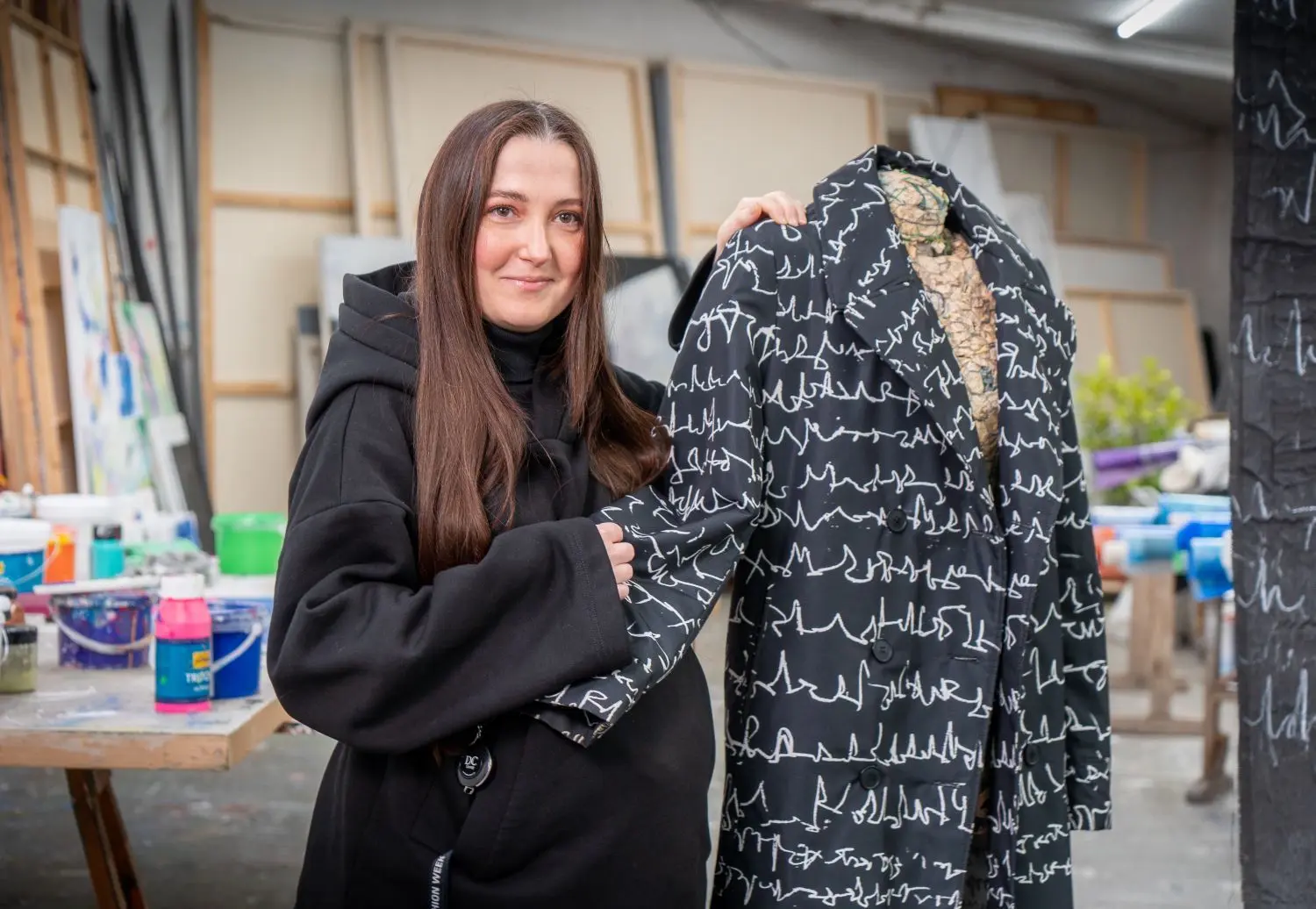 Kateryna Biakova ist hochschwanger. Sie steht neben einem von ihr designten Mantel, der in Kooperation mit der Ulmer Künstlerin Marianne Hollenstein entstanden ist.