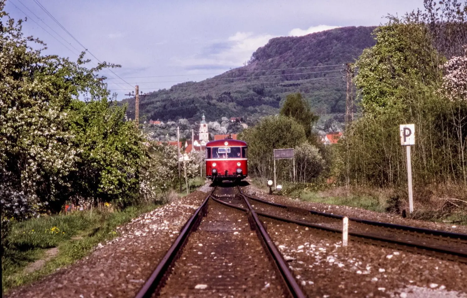 Blick vom Bahnhof in Boll auf einen Zug im Mai 1988. Hinter dem roten Schienenbus ist die Kirche von Dürnau zu sehen.⇥