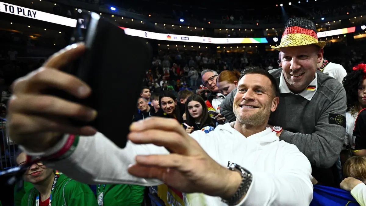Eigentlich ist er ein Publikumsliebling. Doch jetzt wollen ihn Handball-Fans bei den EM-Spielen am liebsten der Halle fernhalten.
20.01.2024, Nordrhein-Westfalen, Köln: Handball: EM, Deutschland - Österreich, Hauptrunde, Gruppe 1, 2. Spieltag, Lanxess Arena. Michael „Mimi“ Kraus macht vor dem Spiel mit Fans ein Selfie. Foto: Tom Weller/dpa +++ dpa-Bildfunk +++