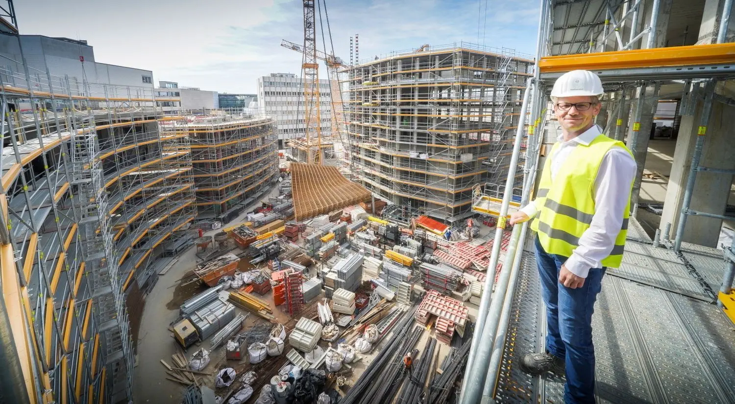 DC-Projektleiter Christoph Röthemeyer schaut sich das Geschehen vom fertigen Rohbau der Sedelhof-Gebäude an der Nordostecke an, links der zentrale Shopping-Komplex. Der neue Albert-Einstein-Platz in der Mitte dient vorläufig noch als Materiallager.⇥