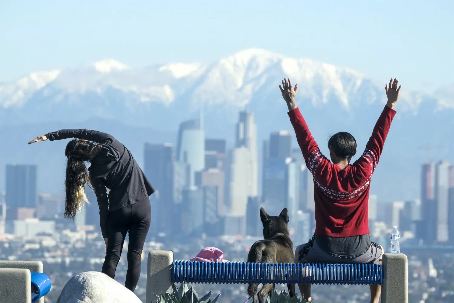 Ein sportliches Paar dehnt sich und beobachtet die San Gabriel Mountains, die hinter der Skyline von LA mit Schnee bedeckt sind.