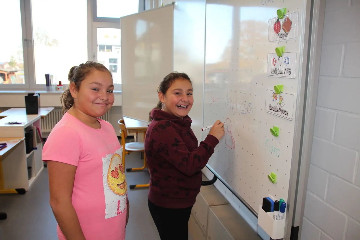 Melissa (rechts) und Selin freuen sich über die neue Tafel in der generalsanierten Käthe-Kollwitz-Schule. Die Klassenzimmer sind bereits fertig eingerichtet (Bild oben rechts), nur wenige Kartons (Bild unten rechts) müssen noch ausgepackt werden. ⇥