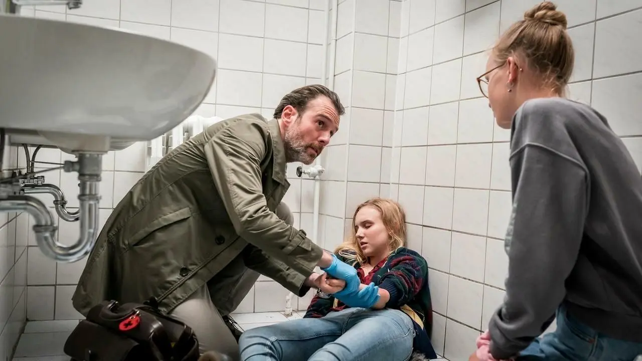Lisa hat ihre bewusstlose Freundin Sarah in der Mädchentoilette gefunden und Dr. Stresow (Benjamin Grüter) zur Hilfe geholt.
