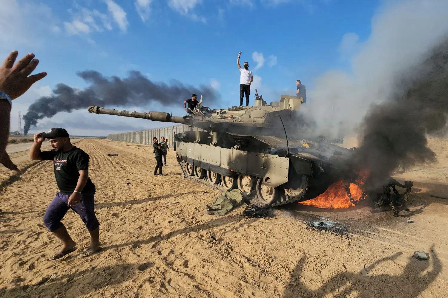 Palästinenser feiern an einem zerstörten israelischen Panzer am Zaun des Gazastreifens.