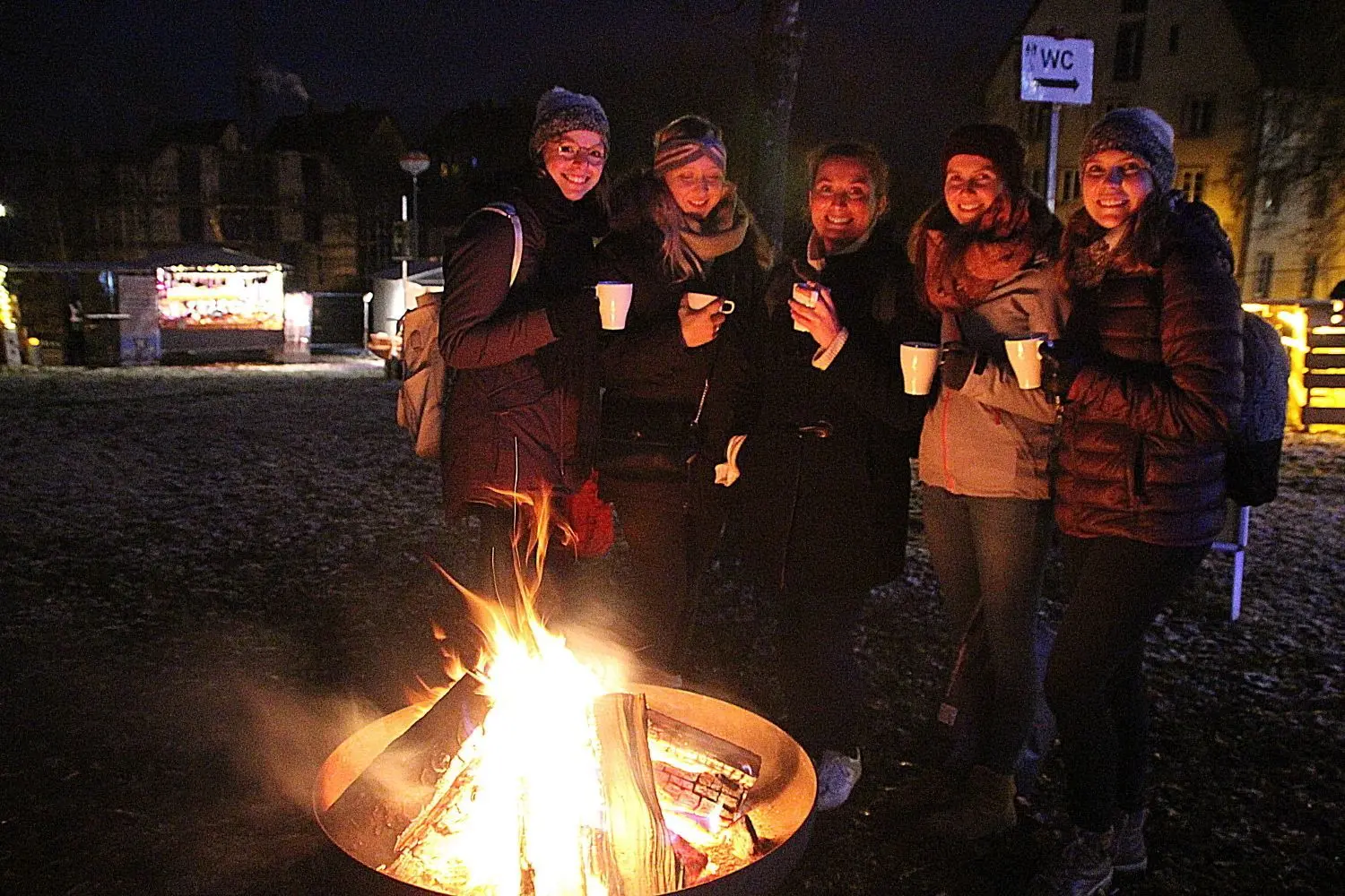 Die Besucherinnen genießen heißen Glühwein am flackernden Lagerfeuer – und erfreuen sich am ersten Schnee. ⇥