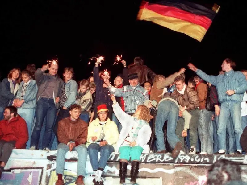 Mit Wunderkerzen in den Händen freuen sich die Menschen auf der Berliner Mauer über die Öffnung der deutsch-deutschen Grenze.