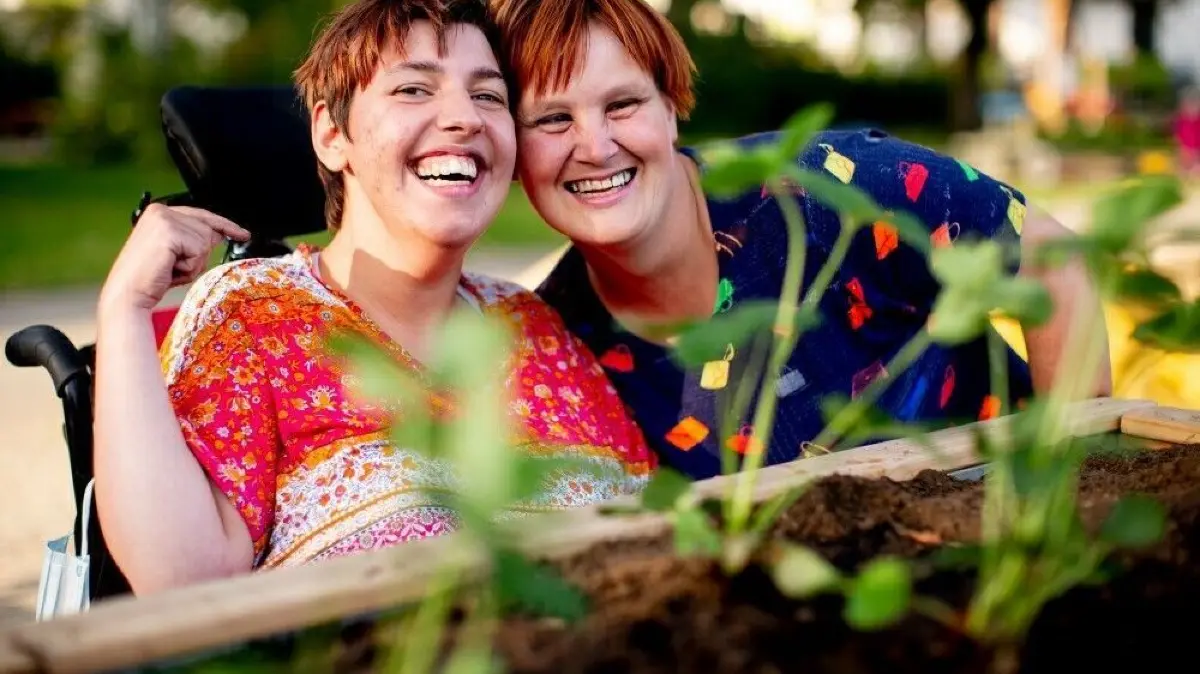 Gewinner*innen sind auch viele Menschen aus den Förderprojekten der Aktion Mensch.
Zwei Bewohnerinnen der Wohngemeinschaft RO 70 in Weimar vor einem rollstuhlgerechten Hochbeet.
Aktion Mensch - 13.09.2021 - Weimar - Gärtnern im Rollstuhl Hochbeet - Nur 20 Minuten am Tag in der Natur sein, hat bereits einen positiven Einfluss auf Körper und Psyche. Kein Wunder also, dass Gartenarbeit für Viele Entspannung pur ist. Das hat sich auch die Wohngemeinschaft „RO 70“ aus Weimar gedacht und mit Fördermitteln der Aktion Mensch barrierefreie Hochbeete aufgebaut – damit alle Bewohner, auch die im Rollstuhl, GEMEINSAM gärtnern können.