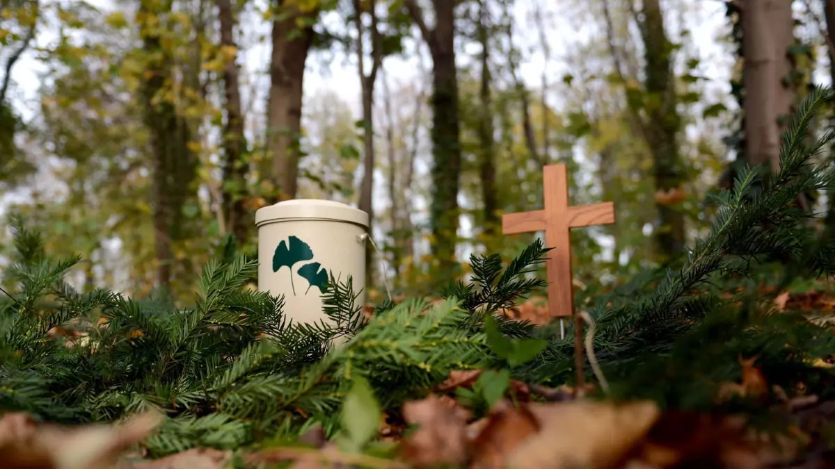 Egal, ob die Bestattung in einem Friedwald oder auf dem Friedhof stattfindet – Angehörige finden bei herkömmlichen Bestattern und mittlerweile auch bei Online-Dienstleister Unternehmen, um den Abschied von einem Toten zu organisieren.
ARCHIV - Eine Musterurne und ein Holzkreuz stehen am 01.11.2013 in einem Friedwald in Berlin. Die Landesforsten beobachten in Niedersachsen einen ungebrochenen Trend zu Waldbestattungen. Seit 2002 hat es mehr als 10 000 Beisetzungen in den Friedwäldern der Landesforsten gegeben. Foto: Britta Pedersen/dpa (zu lni "Trend zur letzten Ruhe im Wald" vom 02.06.2014) +++ dpa-Bildfunk +++