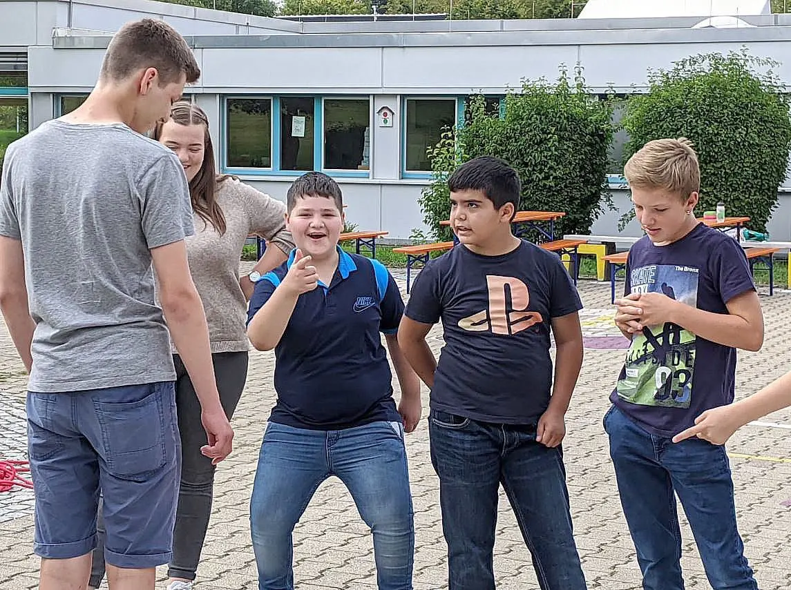 Drei Sommerschüler zusammen mit zwei Jugendbegleitern im Pausenhof.