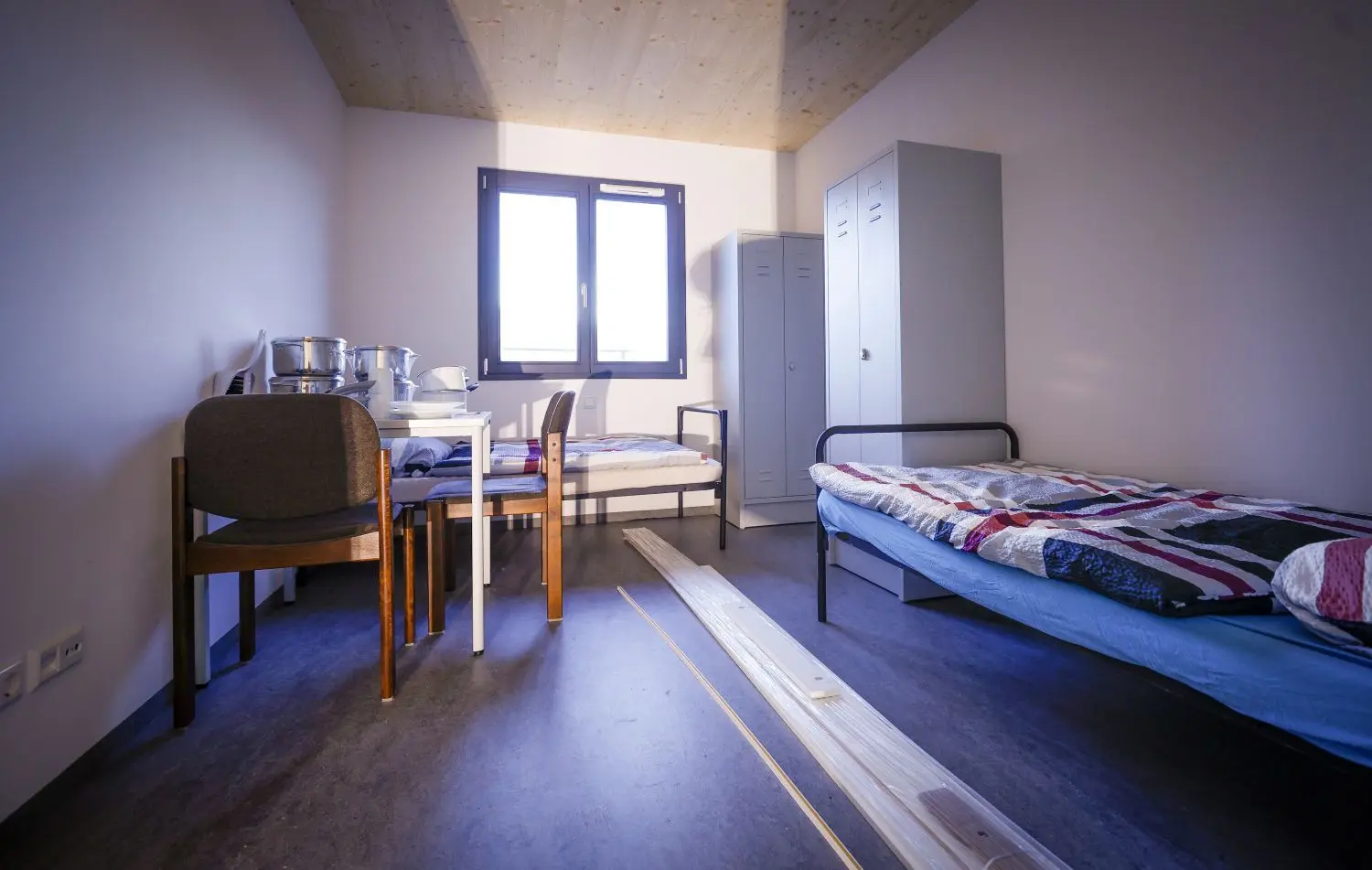 Einblick in eins der beiden Schlafzimmer pro Wohnung: zwei Betten, zwei Schränke, ein Tisch und zwei Stühle.