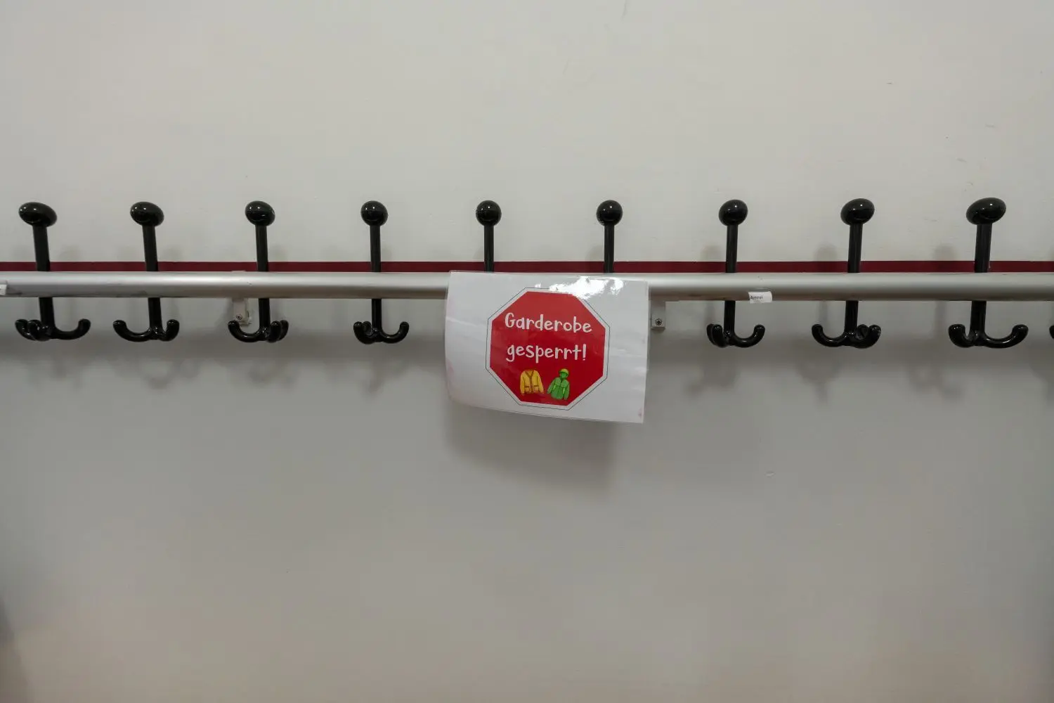 Ein Schild mit der Aufschrift "Garderobe gesperrt" hängt an einer Kleiderhakenstange an einer Schule.