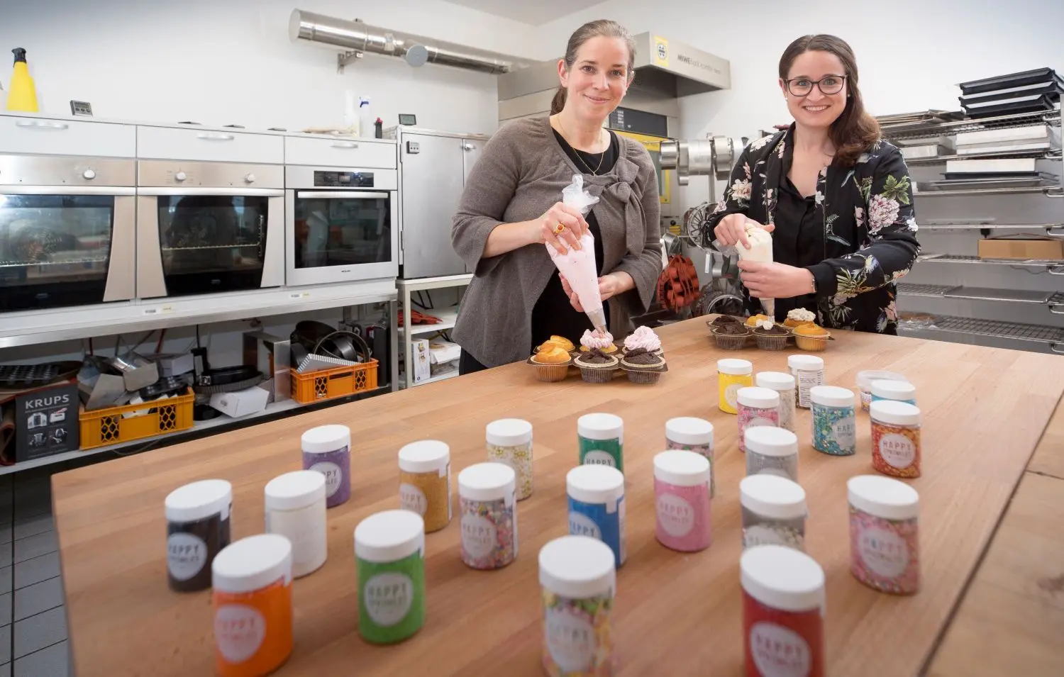 Geschäftsführerin Nathalie Knauer (links) und Marketing-Leiterin Judith Fiedler dekorieren in der Versuchsküche des Hobbybäcker-Versands Cupcakes. Zum Schluss werden die kleinen Küchlein mit bunten Streuseln verziert.⇥
