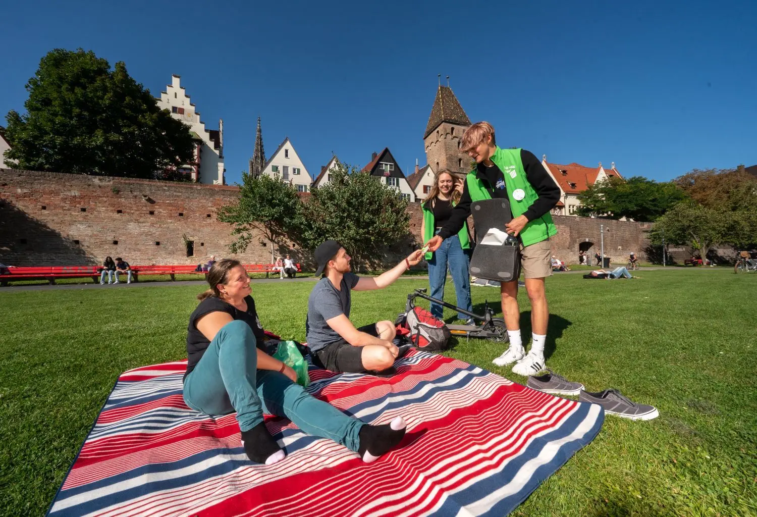 Die Müllscouts Sophia Moisel und Jakob Russo verteilen auf der Donauwiese Geschenke: hier an Christopher Tienes und Julie Miller.