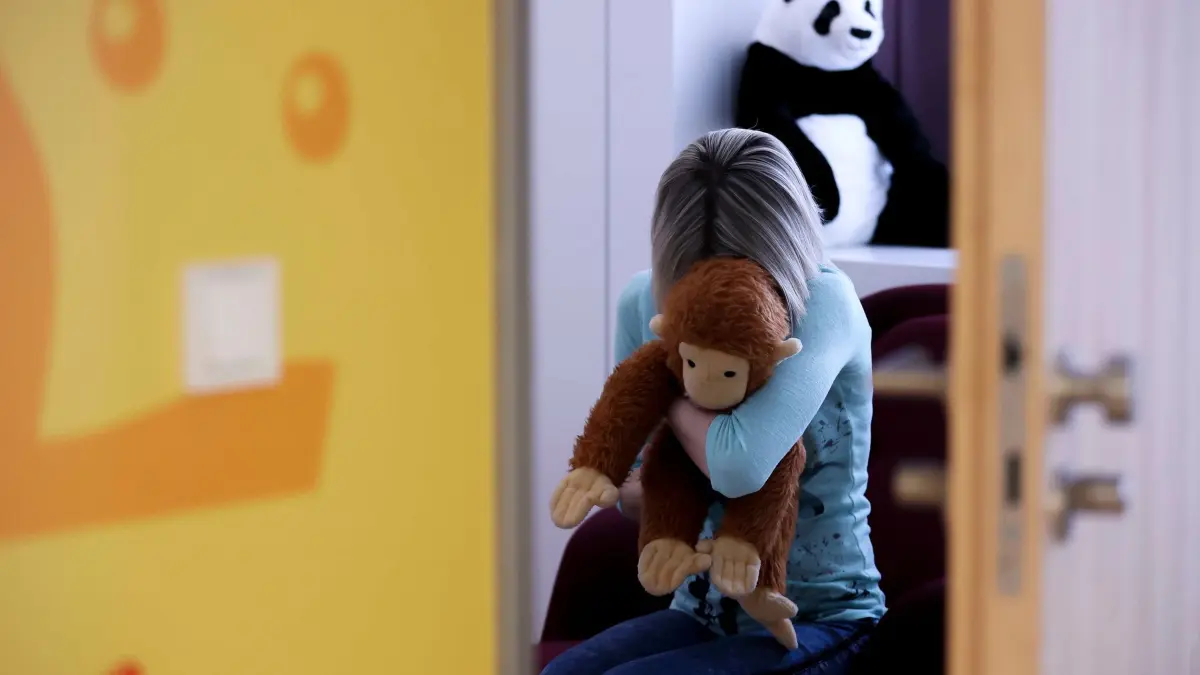 Kind mit Kuscheltier: PRODUKTION - 14.03.2022, Sachsen, Leipzig: ILLUSTRATION - Eine junge Frau sitzt mit einem Kuscheltier im Arm in einem Raum des Childhood House, in dem Kinder und Jugendliche, die von Missbrauchs betroffen sind, vernommen werden können (gestellte Szene). SPD und Grüne wollen ärztlichen Austausch zum Schutz von Kindern stärken. (zu dpa: «SPD und Grüne wollen ärztlichen Austausch zum Kinderschutz stärken») Foto: Jan Woitas/dpa +++ dpa-Bildfunk +++