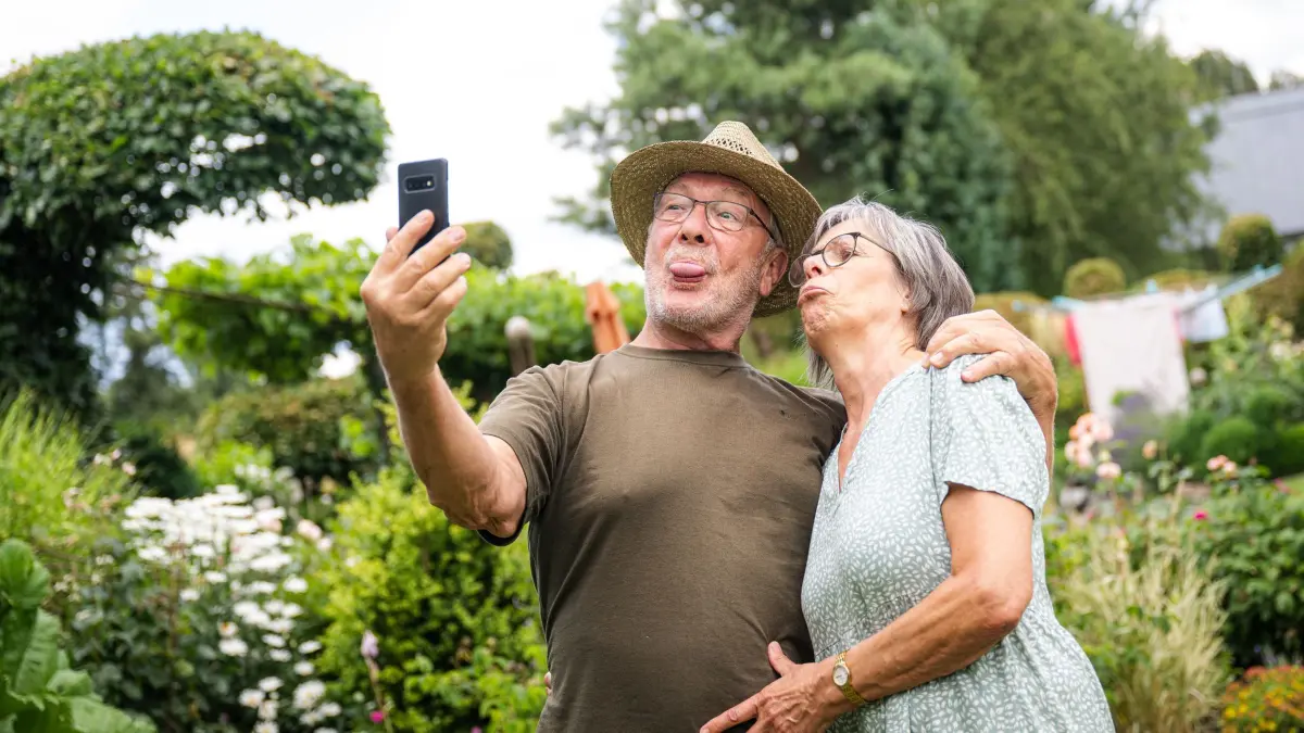 Zwei ältere Menschen nehmen im Garten ein Selfie auf: ILLUSTRATION - Schnappschuss für die Ewigkeit? Wer weiß, aber wer später einen großen Abzug von seinen Handyfotos haben will, achtet besser auf ein paar Einstellungen. (zu dpa: «An die Wand damit: So werden Fotos zu Kunstwerken») Foto: Benjamin Nolte/dpa-tmn/dpa - Honorarfrei nur für Bezieher des dpa-Themendienstes +++ dpa-Themendienst +++
