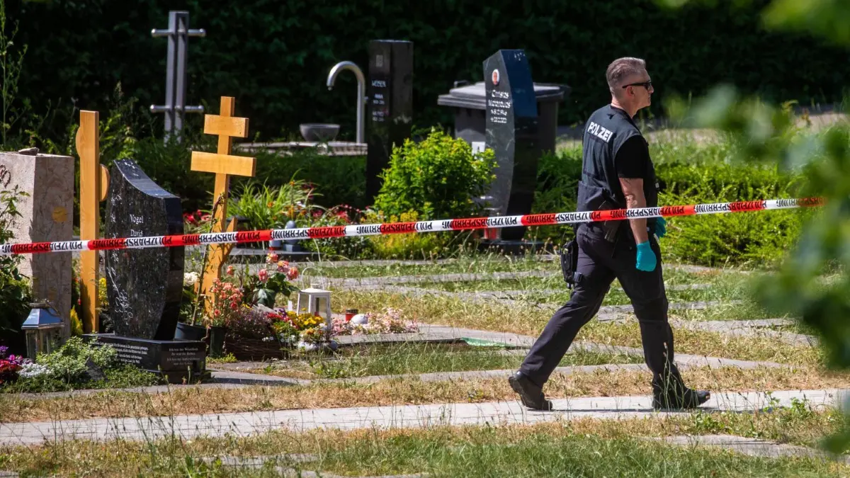 Polizeiabsperrungen am Tatort auf dem Friedhof in Altbach im Juni 2023, wo die Handgranate während einer Trauerfeier hochging.
ARCHIV - 09.06.2023, Baden-Württemberg, Altbach: Ein Polizist geht über den abgesperrten Teil an einem Tatort auf einem Friedhof. Durch den Wurf eines explodierenden Gegenstands auf eine Trauergemeinde gab es mehrere Verletzte. Wegen des Handgranatenwurfs auf eine Trauergemeinde in Altbach nahe Stuttgart müssen sich in mehreren Prozessen der mutmaßliche Werfer und fünf Männer vor dem Landgericht Stuttgart verantworten. Sie sollen den mutmaßlichen Haupttäter auf seiner Flucht gefasst und verprügelt haben (zu dpa: «Weitere Prozesse nach Anschlag mit Handgranate und Prügelei in Altbach») Foto: Christoph Schmidt/dpa +++ dpa-Bildfunk +++