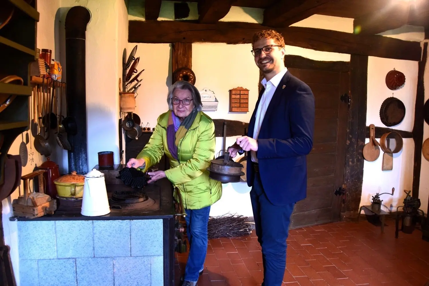 Die Rosenküchle sind ein traditionelles Gebäck der schwäbischen Küche. Der Grundteig besteht aus Milch, Mehl, Zucker, Salz und Eiern. Annemarie Fröhlich präsentiert das spezielle Roseneisen zur Herstellung. Bürgermeister Simon Baier schaut interessiert zu.⇥