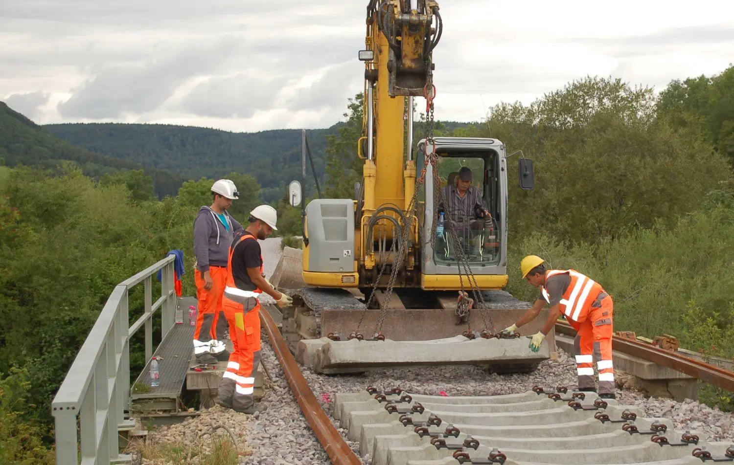 Eine Betonschwelle nach der anderen wird auf den Bahndamm gesetzt. Ein Großteil der Arbeit, so versteht es der Laie, besteht aber darin, das Gleisbett zu schaffen, alten Schotter auszuräumen und neuen einzubringen. ⇥