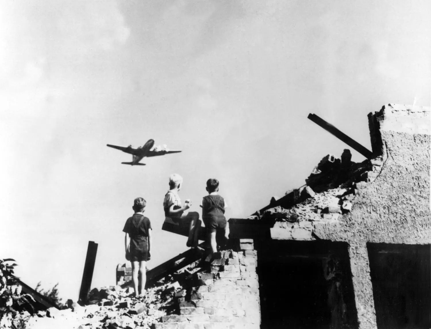 Kinder auf Trümmern beobachten 1948 eines der vielen US-Transportflugzeuge, die während der Blockade überlebenswichtige Care-Pakete nach West-Berlin bringen. Die Dankbarkeit der Bevölkerung ist groß. Als Reaktion auf die Währungsreform in den Westsektoren haben die Sowjets fast elf Monate lang alle Land- und Wasserwege dorthin gesperrt – bis zum 12. Mai 1949.⇥⇥
