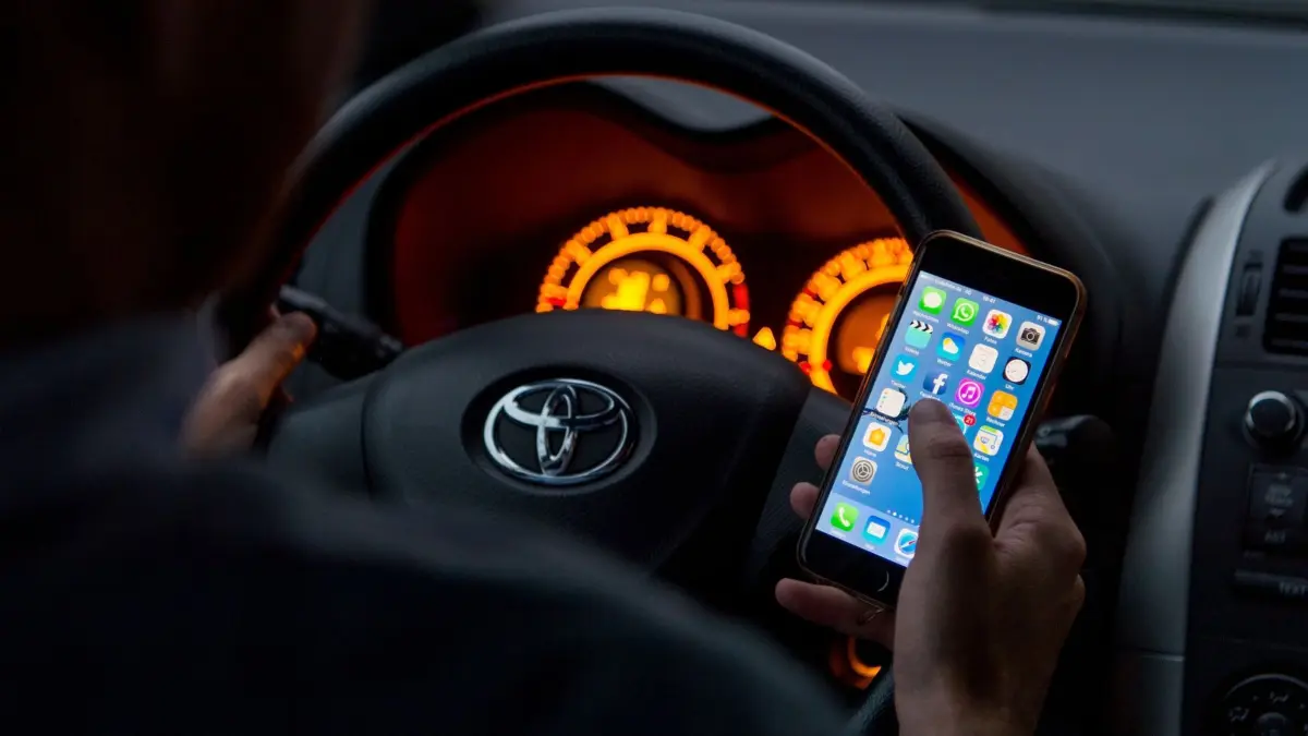 Ein Mann sitzt mit Handy in der Hand in einem Auto am Steuer