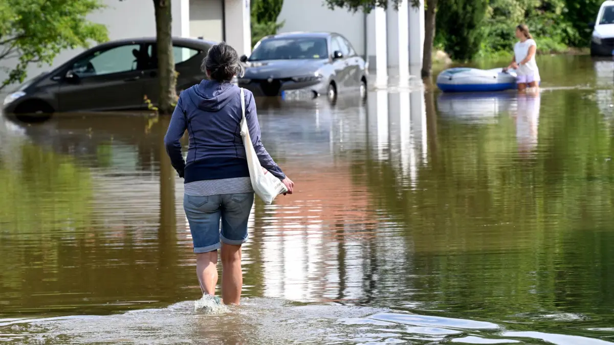 Hochwasser in Bayern — Fahrenzhausen: 02.06.2024, Bayern, Fahrenzhausen: Eine Frau watet durch eine überschwemmte Straße in einem Wohngebiet. Nach starken Regenfällen gibt es in der Region Hochwasser mit Überschwemmungen. Foto: Felix Hörhager/dpa +++ dpa-Bildfunk +++