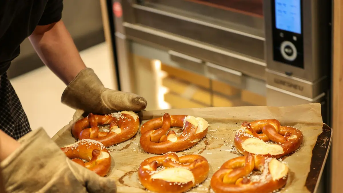 ARCHIV - 26.06.2023, Sachsen, Leipzig: Ein Mitarbeiter nimmt ein Blech mit Brezeln aus dem Backofen einer Bäckerei. Immer mehr Mittelständler in Deutschland sehen sich angesichts der Dauerkrisen der vergangenen Jahre zu grundlegenden Anpassungen im eigenen Unternehmen gezwungen. (zu dpa «Mittelstand sorgt sich um Wettbewerbsfähigkeit Deutschlands») Foto: Jan Woitas/dpa +++ dpa-Bildfunk +++