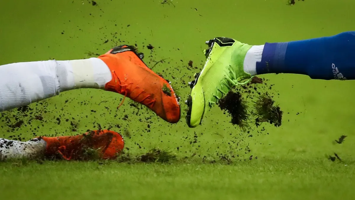 Fußballschuhe: ARCHIV - 30.01.2019, Hamburg: Fußball: 2. Bundesliga, Hamburger SV - SV Sandhausen, 19. Spieltag im Volksparkstadion. Gras fliegt um die Fußballschuhe zweier Spieler bei einem Zweikampf. (zu dpa: «Fußballschuhe aus dem Ofen? Firma punktet mit Aufwärmgerät») Foto: Christian Charisius/dpa +++ dpa-Bildfunk +++