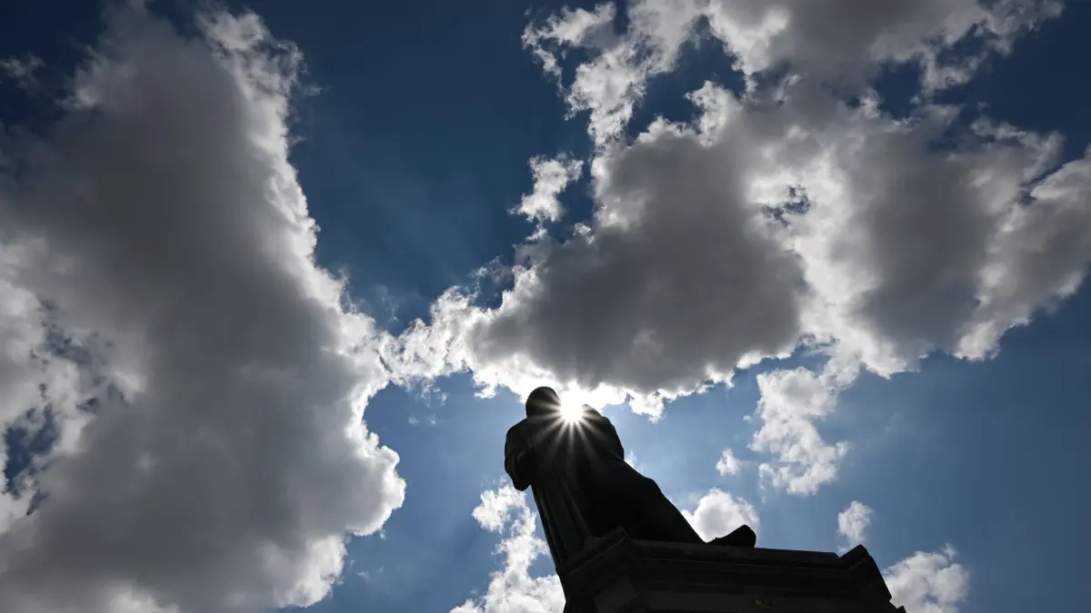 Sonne und Wolken wechseln sich in der ersten Ferienwoche ab.: ARCHIV - 21.07.2022, Rheinland-Pfalz, Mainz: Die Sonne strahlt von einem bewölkten Himmel auf das Gutenberg-Denkmal in der Innenstadt. (zu dpa: «Wetter am Wochenende wird unbeständig») Foto: Arne Dedert/dpa +++ dpa-Bildfunk +++