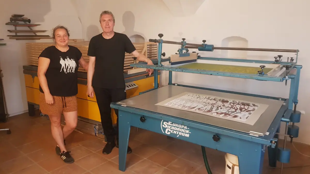 Adela Knajzl und Patrick Nicolas neben der großen Siebdruckmaschine in der Griesbadgalerie. Im Hintergrund ist der Belichter zu sehen.